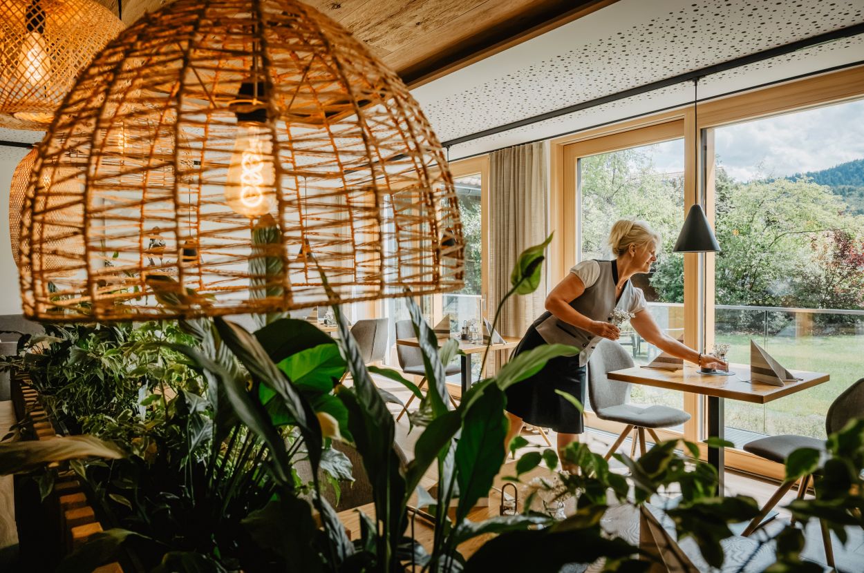 Detail Restaurant mit Korbleuchte und Mitarbeiterin Detail aus dem Restaurant mit Korbleuchte und Planzen, im Hintergrund Mitarbeiterin die Tisch deckt